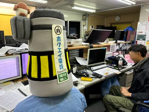 ホクエイ電設のロゴが入った電柱の被り物と事務所の様子