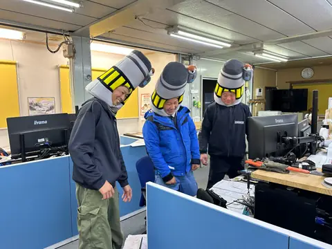 事務所で電柱の被り物をしてふざける社員たち