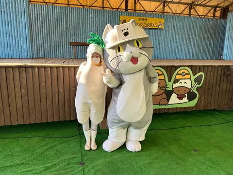 ゆるキャラと並んで写る大根の着ぐるみ姿の社員